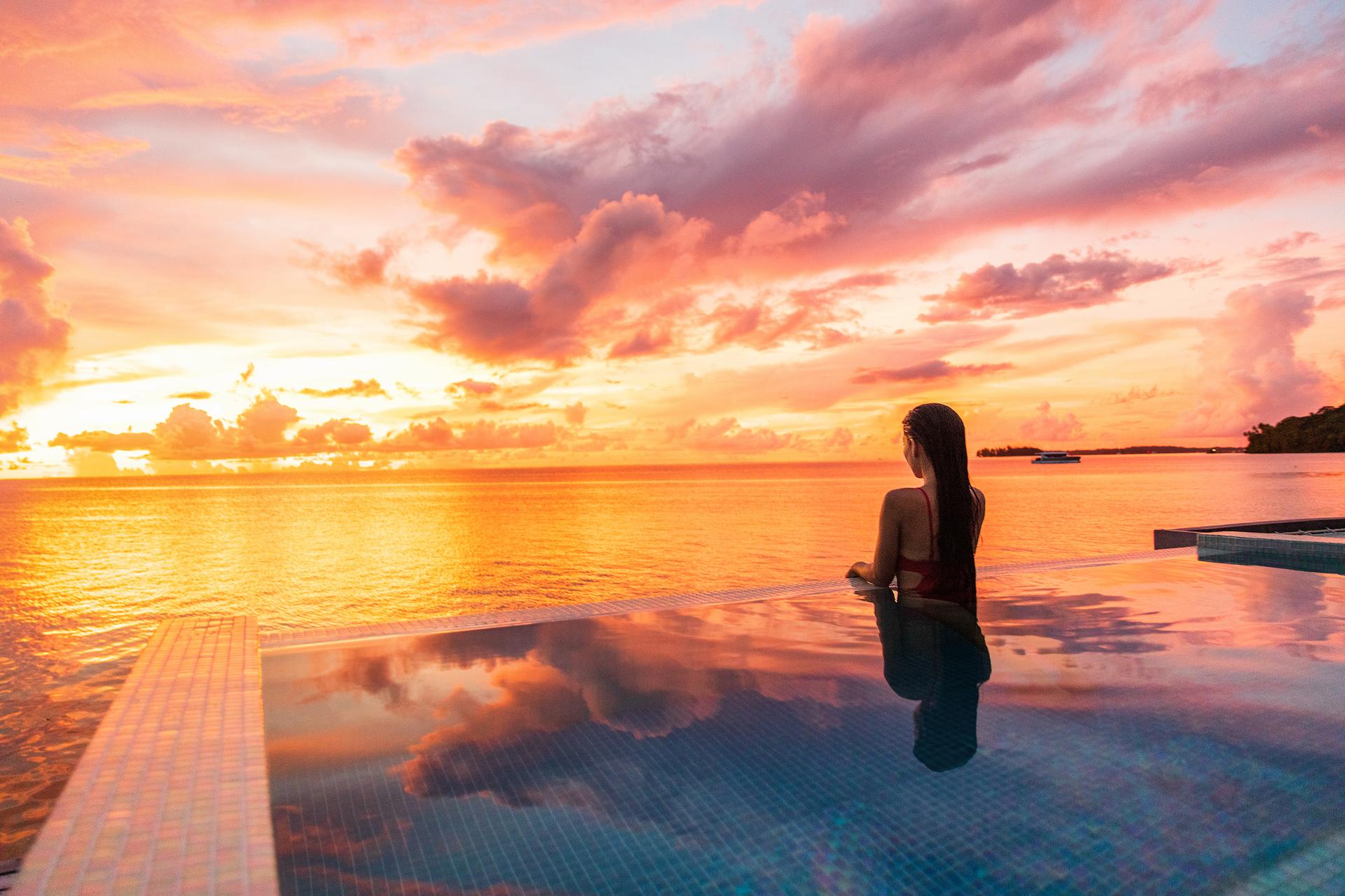 Paradise sunset idyllic vacation woman silhouette swimming in infinity pool looking at sky reflections over ocean dream. Perfect amazing travel destination in Bora Bora, Tahiti, French Polynesia.