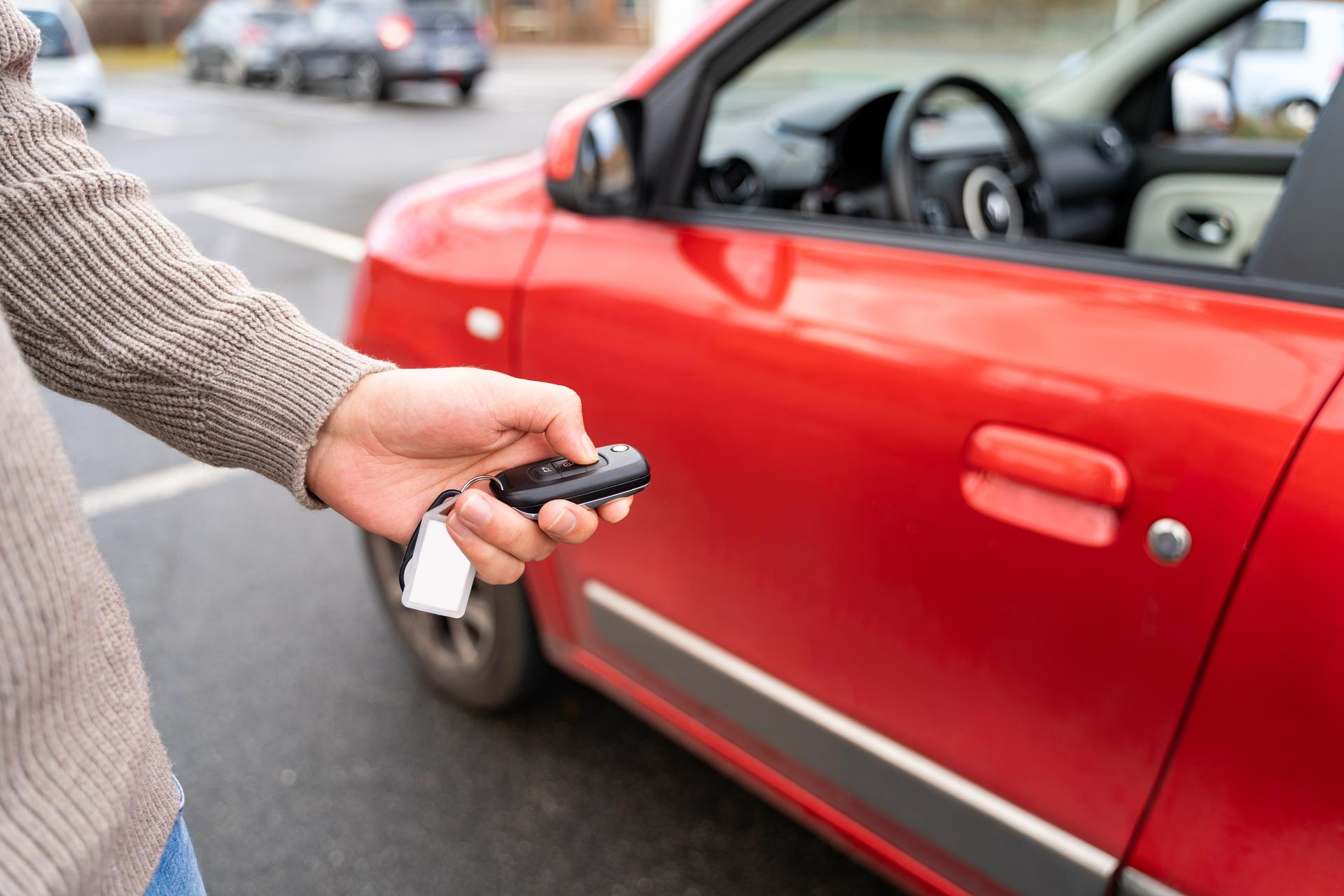 Male hand holding electronic remote key pushing button near red rental car